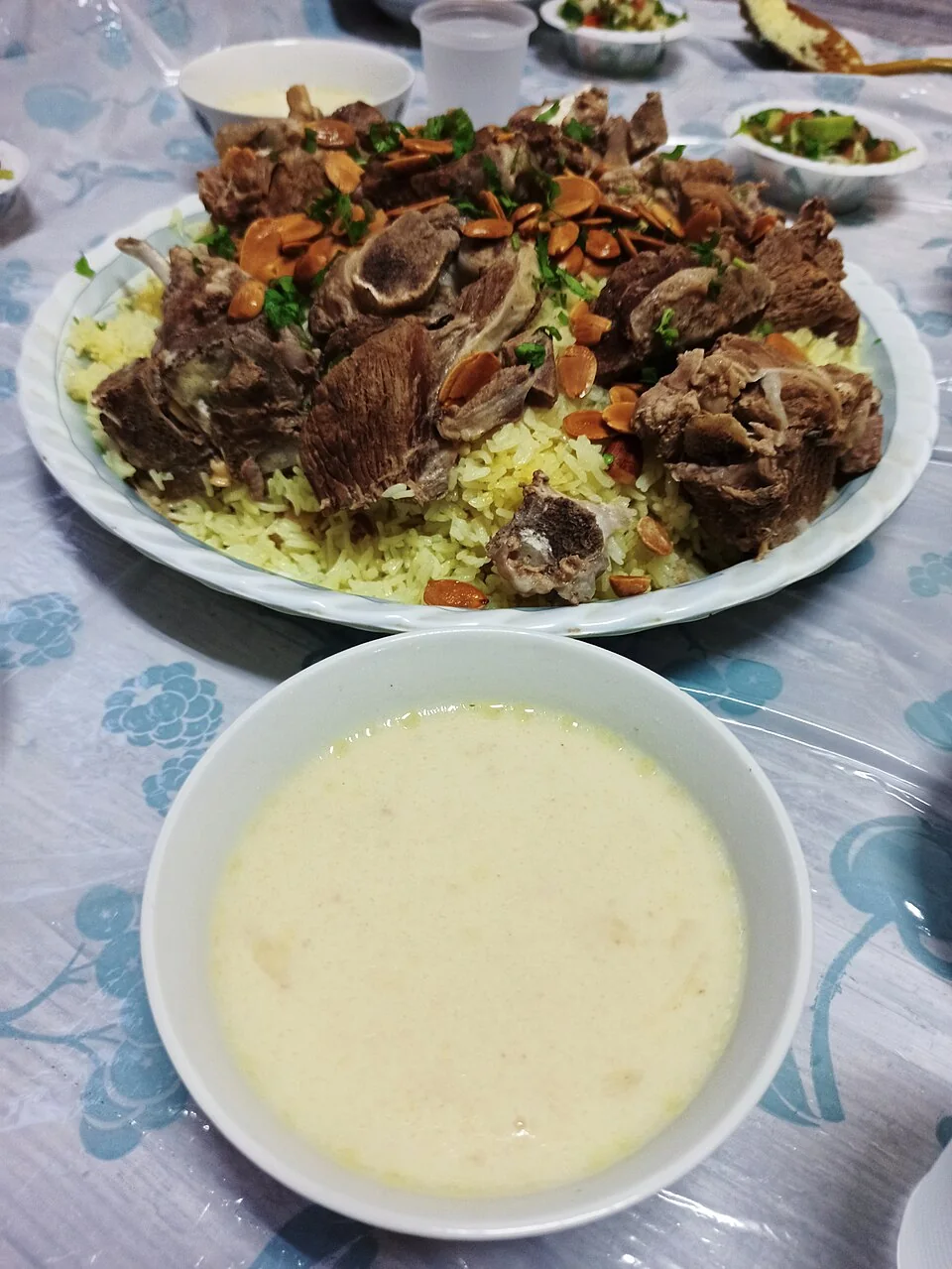 밥과 고기, 아몬드를 담은 만사프 접시와 앞쪽의 요거트 국물 그릇