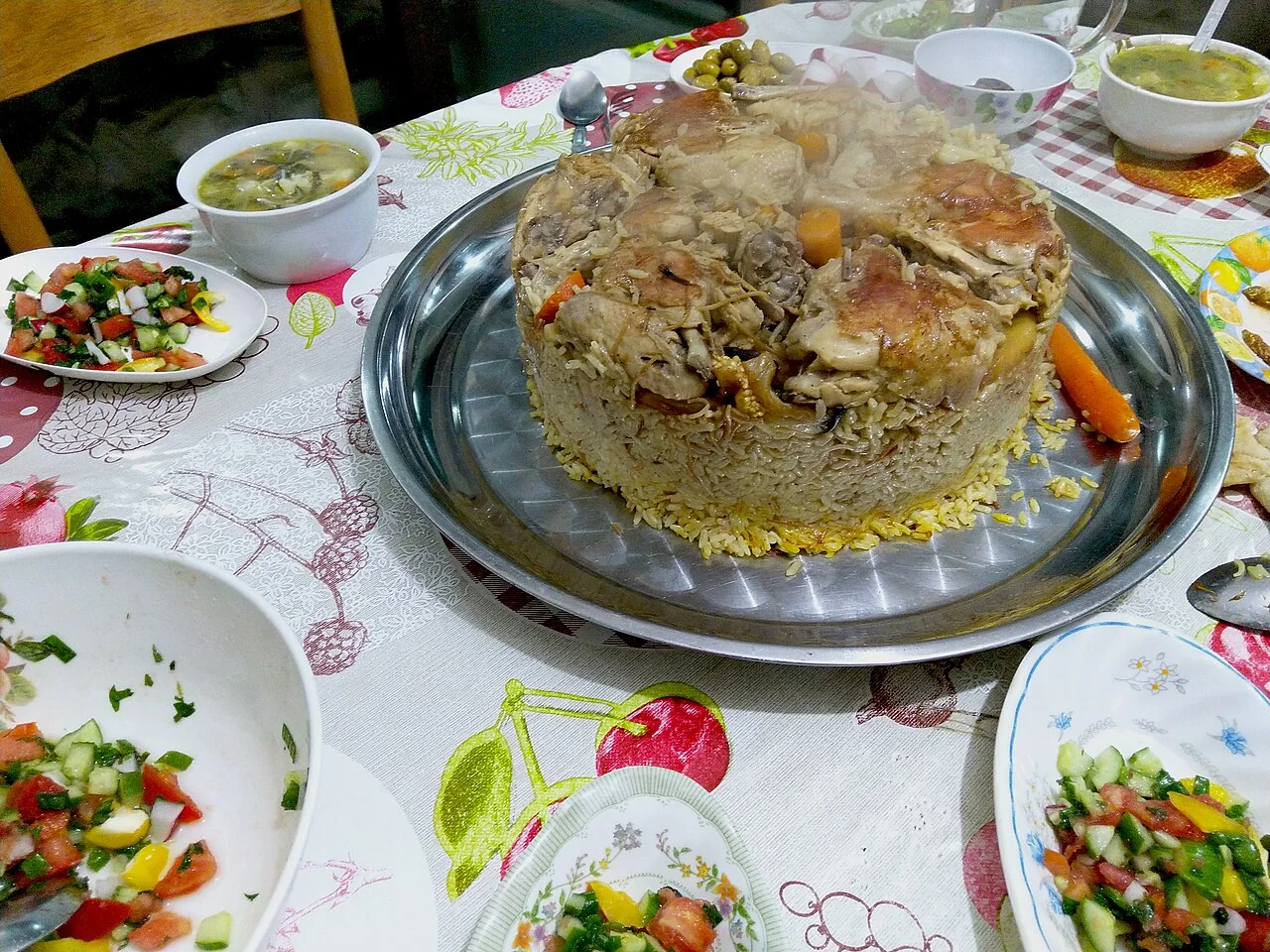 둥근 금속 쟁반 위에 냄비 모양으로 뒤집어 담은 마끌루바와 주변의 샐러드 그릇